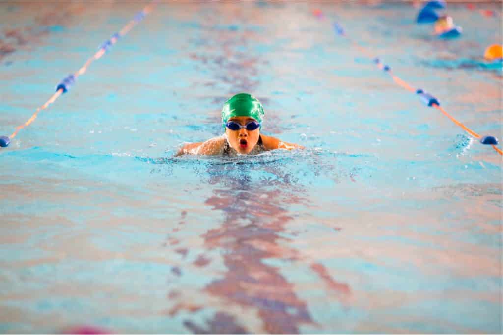 Girl with swimming cap and goggles takes breath while swimming in pool